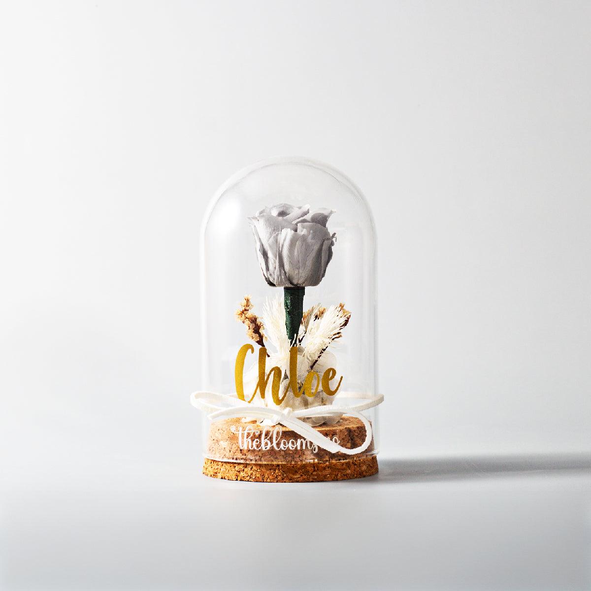 Modern grey preserved rose in a clear glass dome with neutral dried flower accents and ribbon detail. Unique and elegant gift from TheBlooms.co, great for minimalist decor lovers or meaningful celebrations.