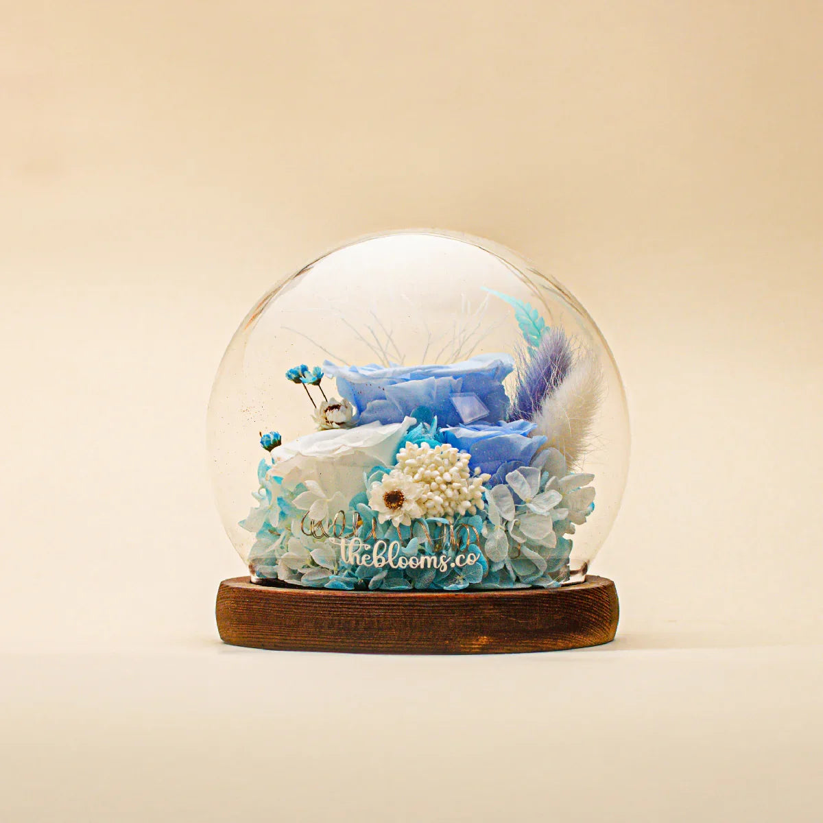 Oceanic Dream preserved flower dome featuring blue and white roses, blue hydrangeas, and a bunny tail accent on a dark wood base.