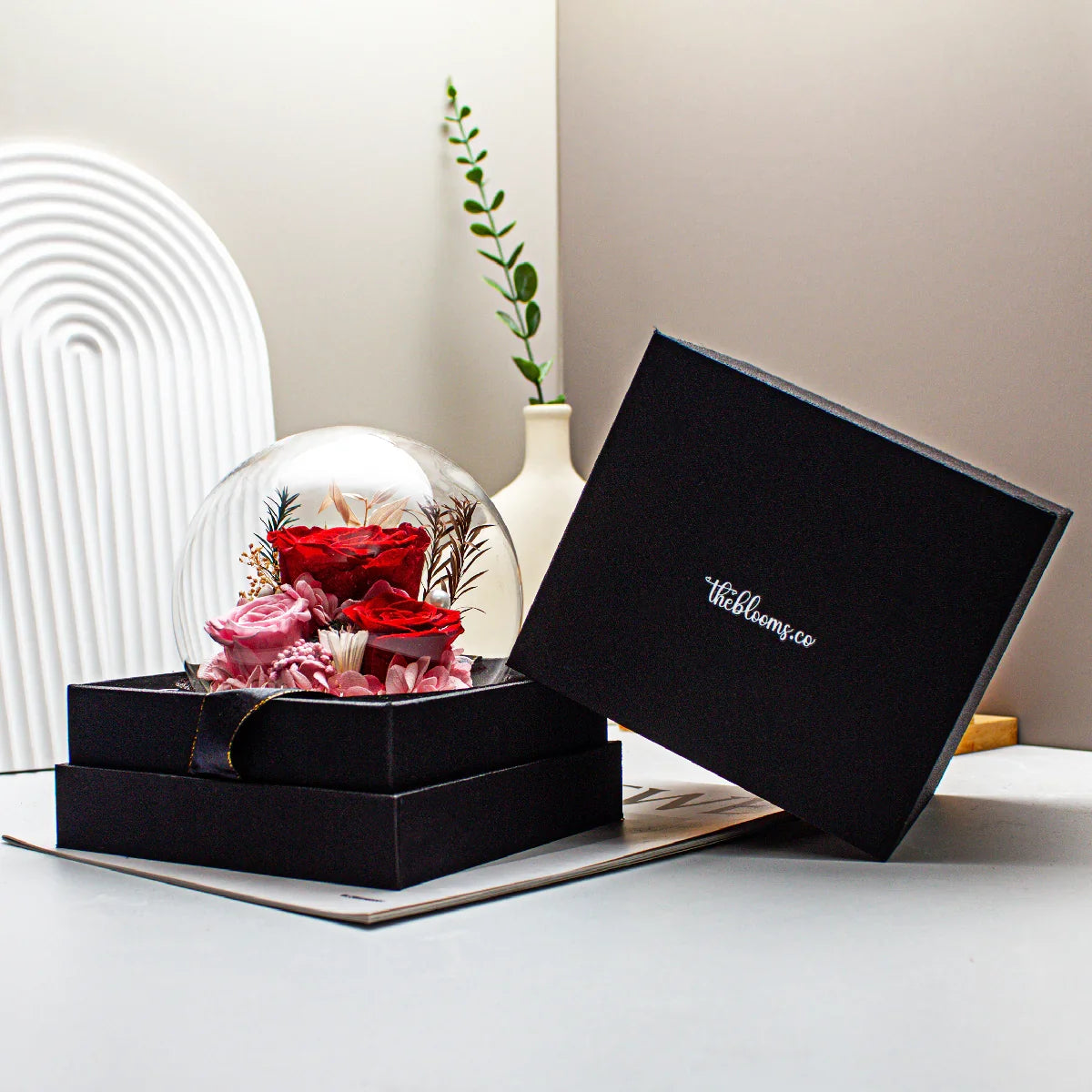 Queen of Hearts preserved flower arrangement in a glass cloche with vibrant red and pink roses, presented in a black theblooms.co gift box.