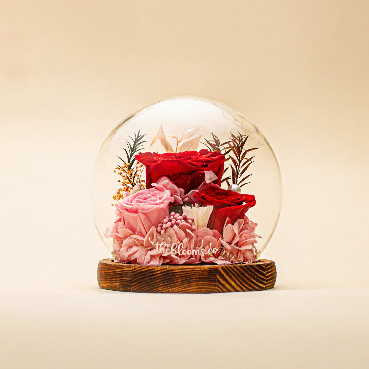 Queen of Hearts preserved flower dome with deep red and blush pink roses, pink hydrangeas, and botanical accents on a dark wood base.
