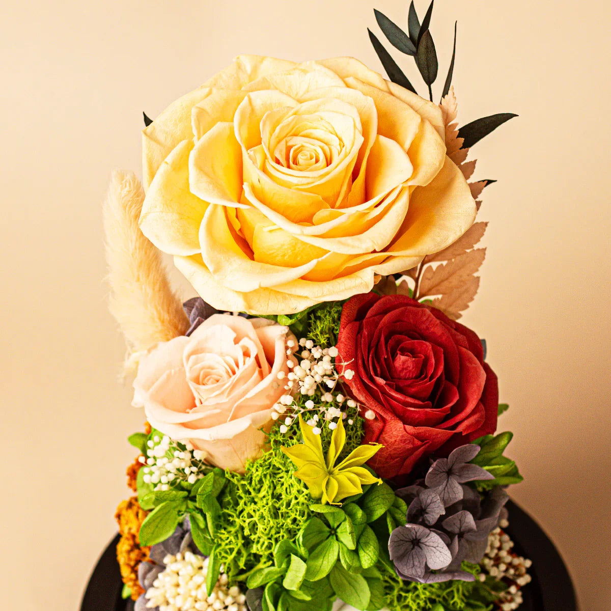 Close-up of a preserved floral arrangement with yellow, red, and pink roses and greenery inside a glass dome.