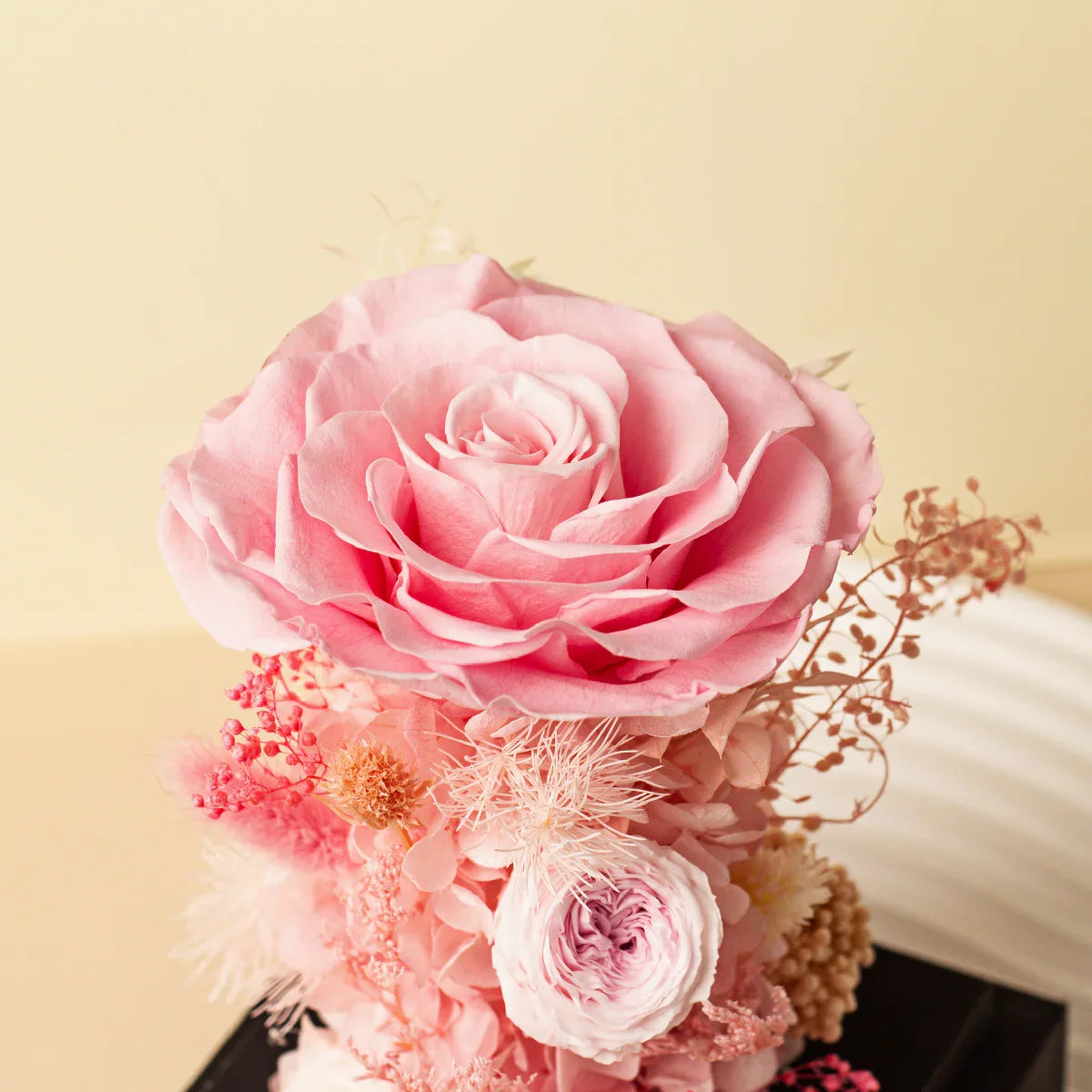 Close-up of a large pink preserved rose at the top of a floral arrangement, surrounded by various smaller pink and white dried flowers.