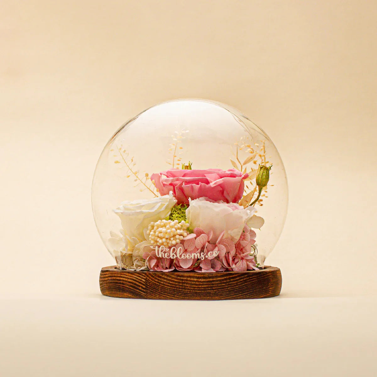 The Enchanted Rose preserved flower dome featuring a signature pink rose and ivory blossoms with delicate pink hydrangeas on a dark wood base.