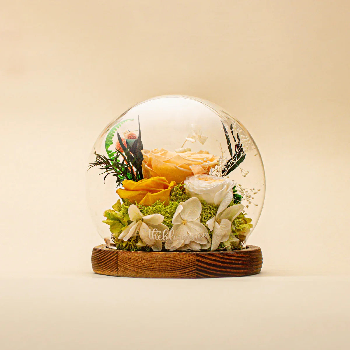 The Secret Garden preserved flower dome featuring yellow, peach, and white roses with green moss and hydrangea accents on a dark wood base.